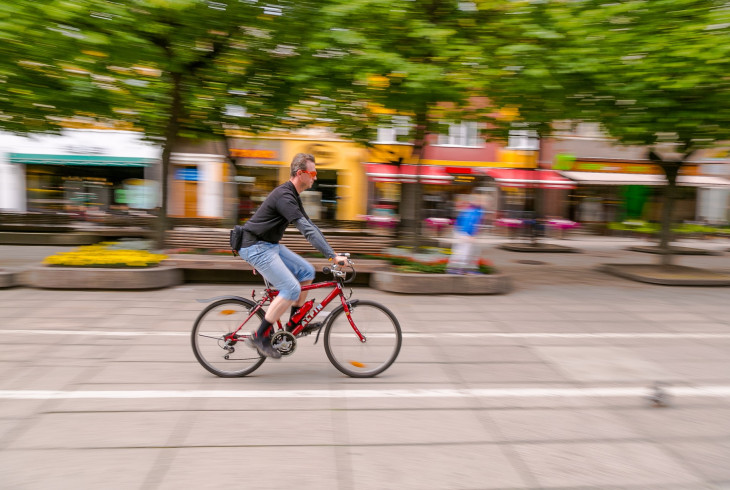 Cyklista na bicykli jazdí po vyhradenej ceste pre cyklistov cez mesto so stromami v pozadí
